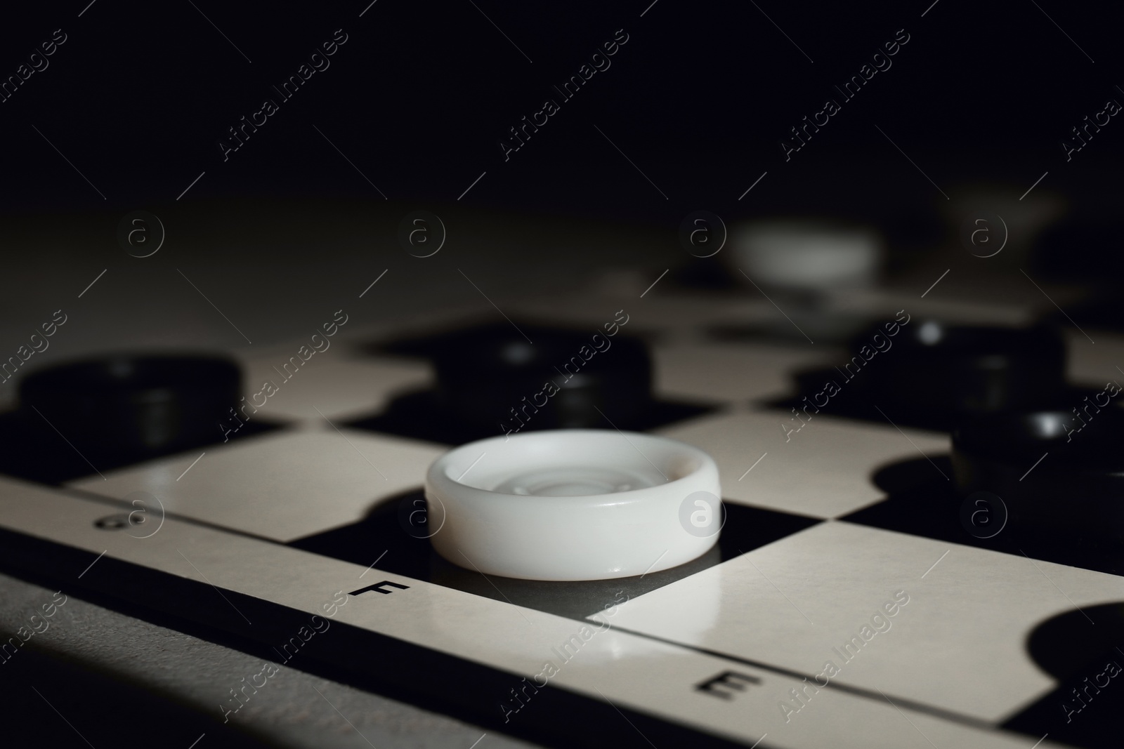 Photo of Checkerboard with game pieces on dark background, closeup