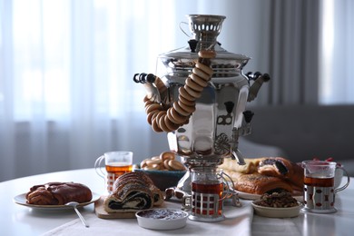 Photo of Traditional Russian samovar with treats on white table at home