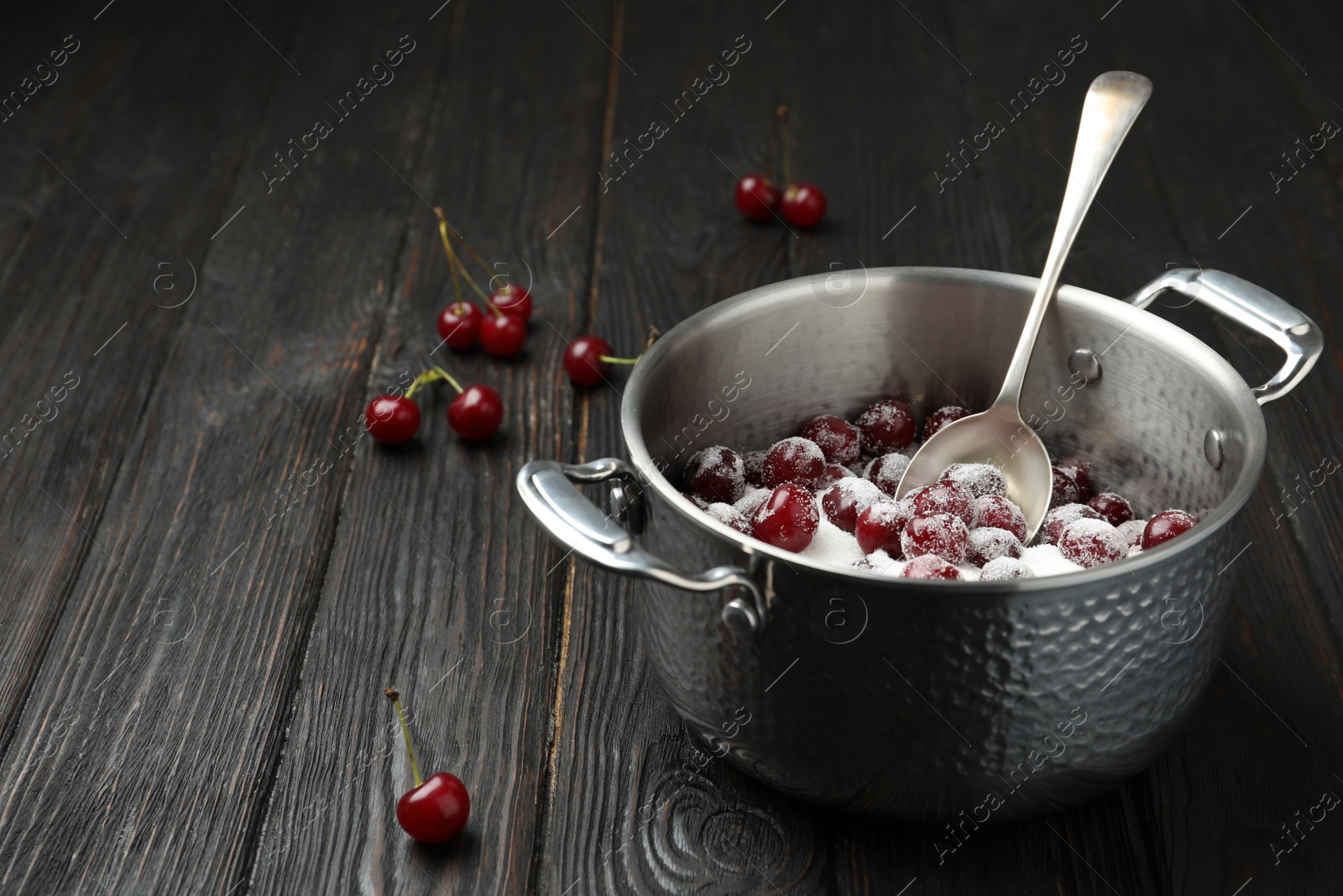 Photo of Pot with cherries and sugar on black wooden table, space for text. Making of delicious jam