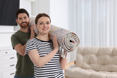 Smiling couple holding rolled carpet in room, space for text