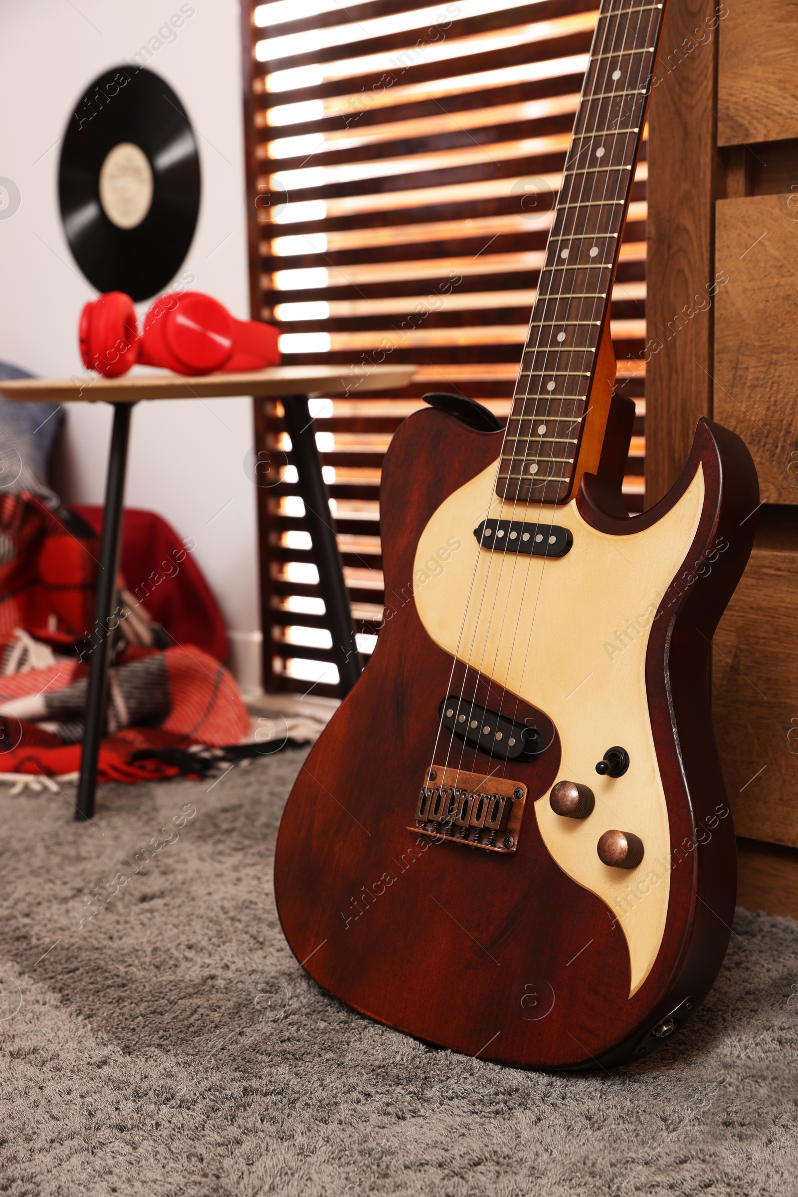 Photo of Stylish guitar and red headphones on wooden table in teenager's room