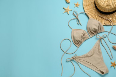 Stylish beige bikini, hat and starfishes on light blue background, flat lay. Space for text