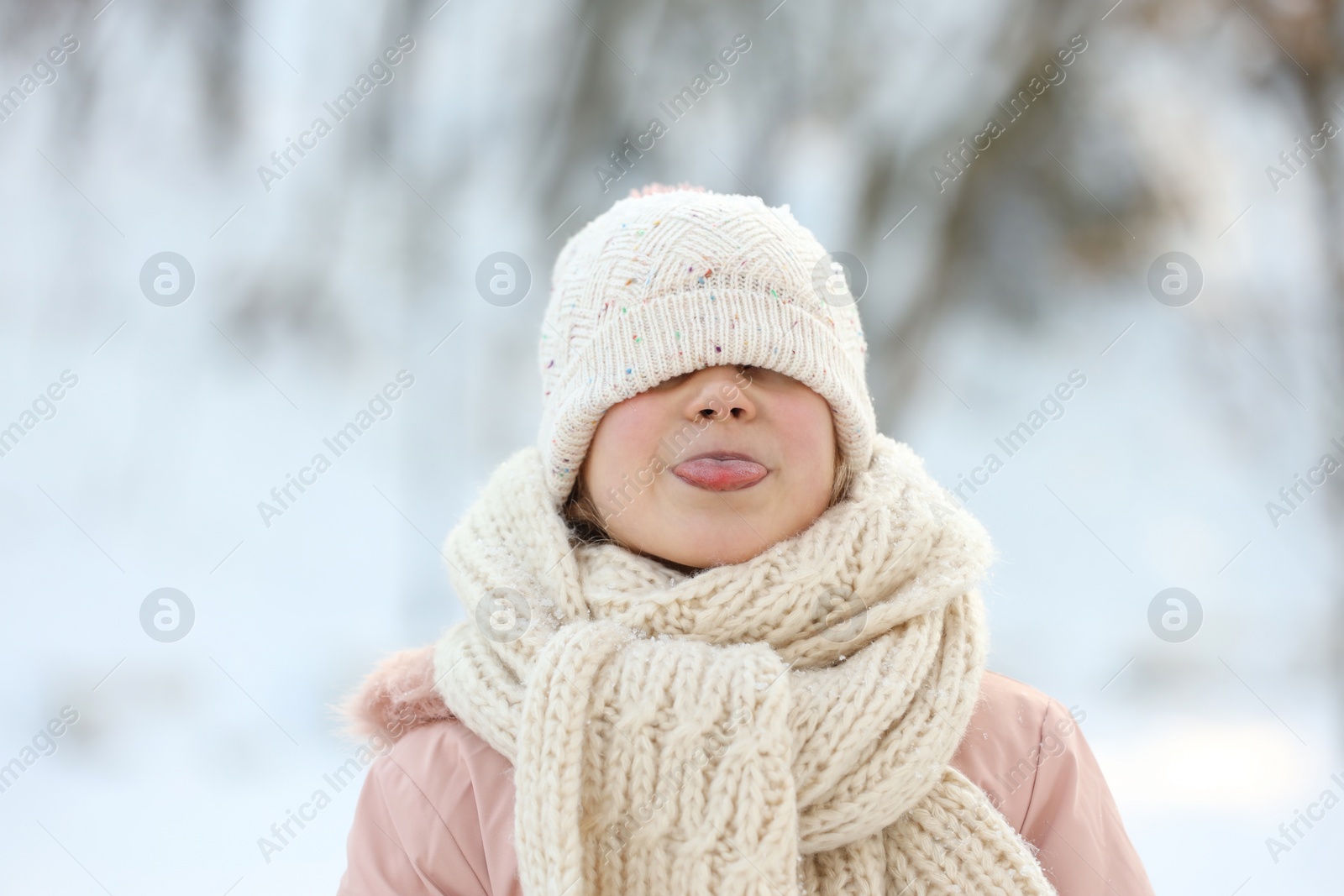 Photo of Cute little girl showing her tongue in snowy park on winter day