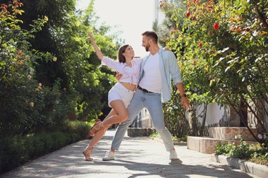 Lovely young couple dancing together in park on sunny day