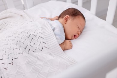 Photo of Cute newborn baby sleeping under white plaid in crib