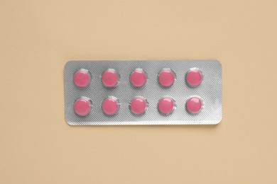 Photo of Pink pills in blister on beige background, top view