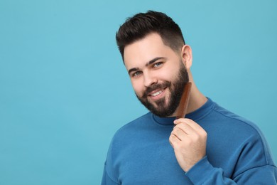 Photo of Handsome young man combing beard on light blue background. Space for text