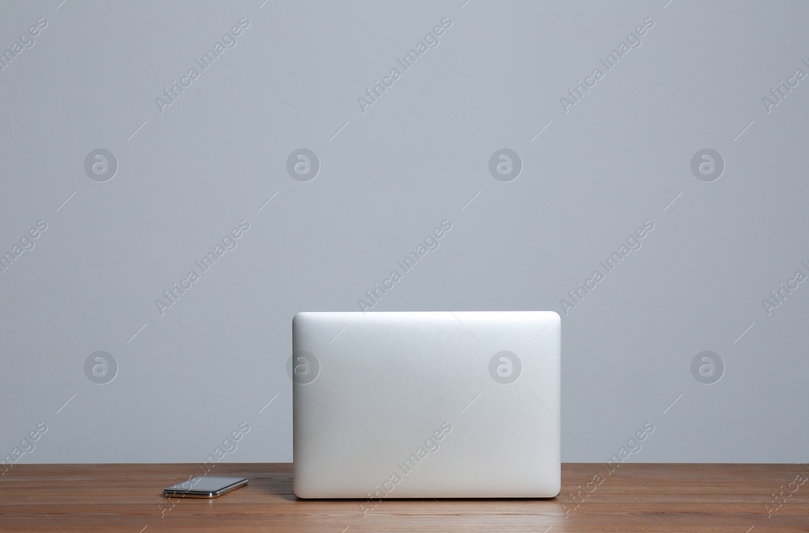 Photo of Modern laptop and mobile phone on wooden table against gray background