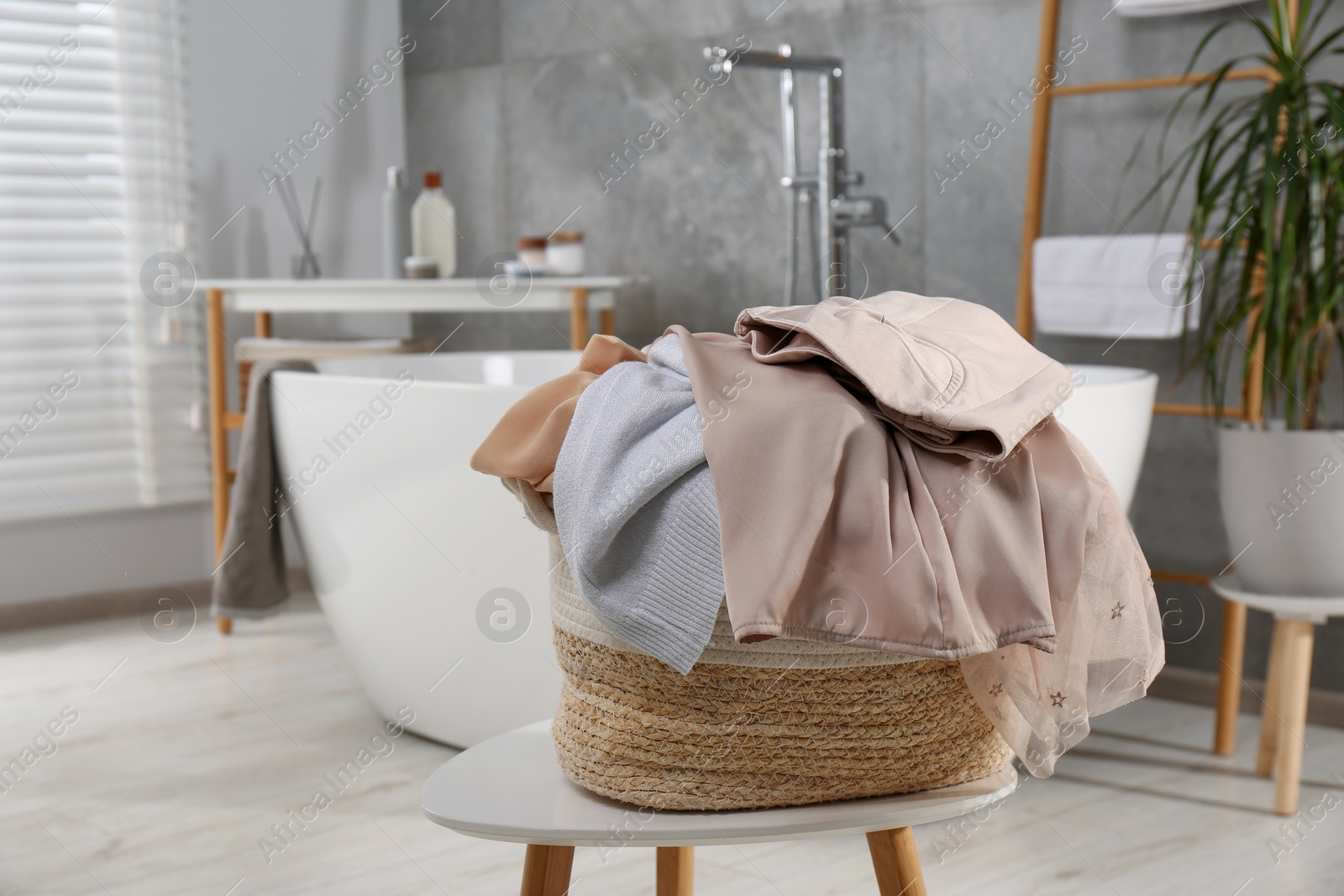 Photo of Wicker laundry basket with clothes on stool in bathroom