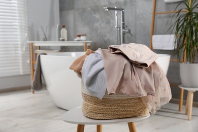 Wicker laundry basket with clothes on stool in bathroom