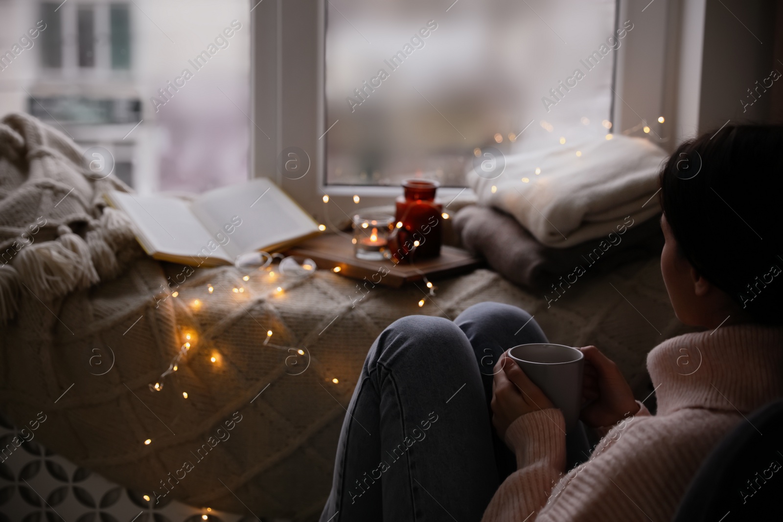 Photo of Woman with hot drink relaxing near window at home. Cozy season