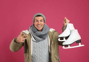 Emotional man with ice skates on pink background