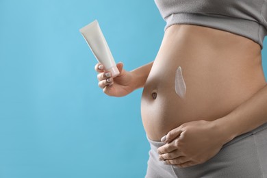 Photo of Pregnant woman with cosmetic product on light blue background, closeup. Space for text