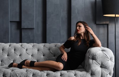 Beautiful woman in elegant dress on sofa indoors. Luxury lifestyle