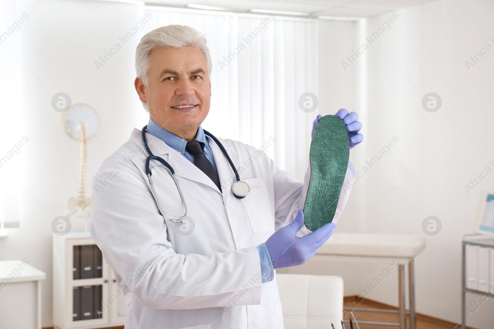 Photo of Senior male orthopedist showing insole in clinic