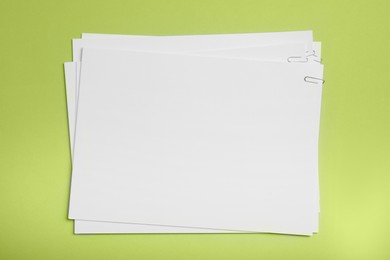 Sheets of paper with clips on light green background, top view