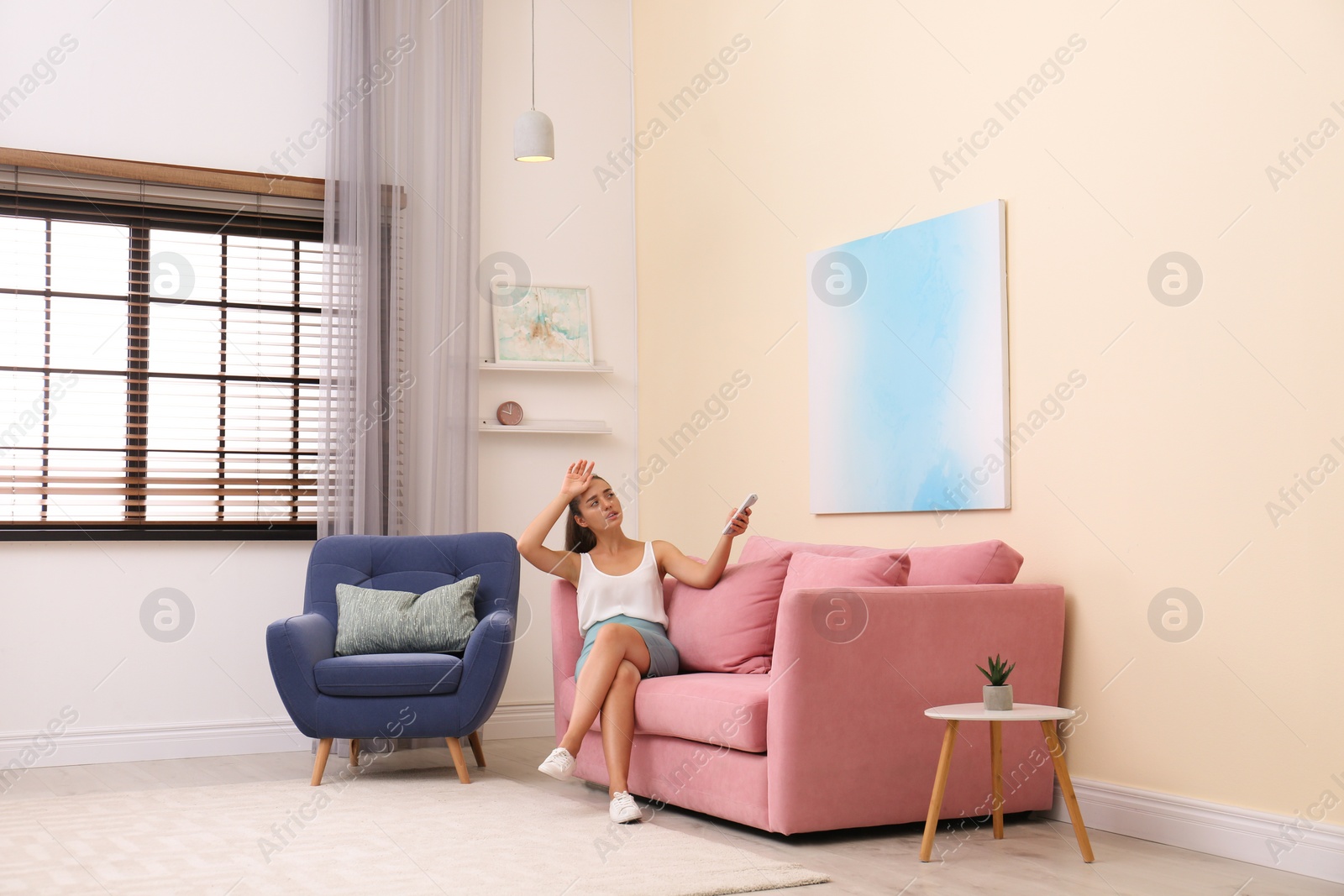 Photo of Young woman switching on air conditioner with remote control at home