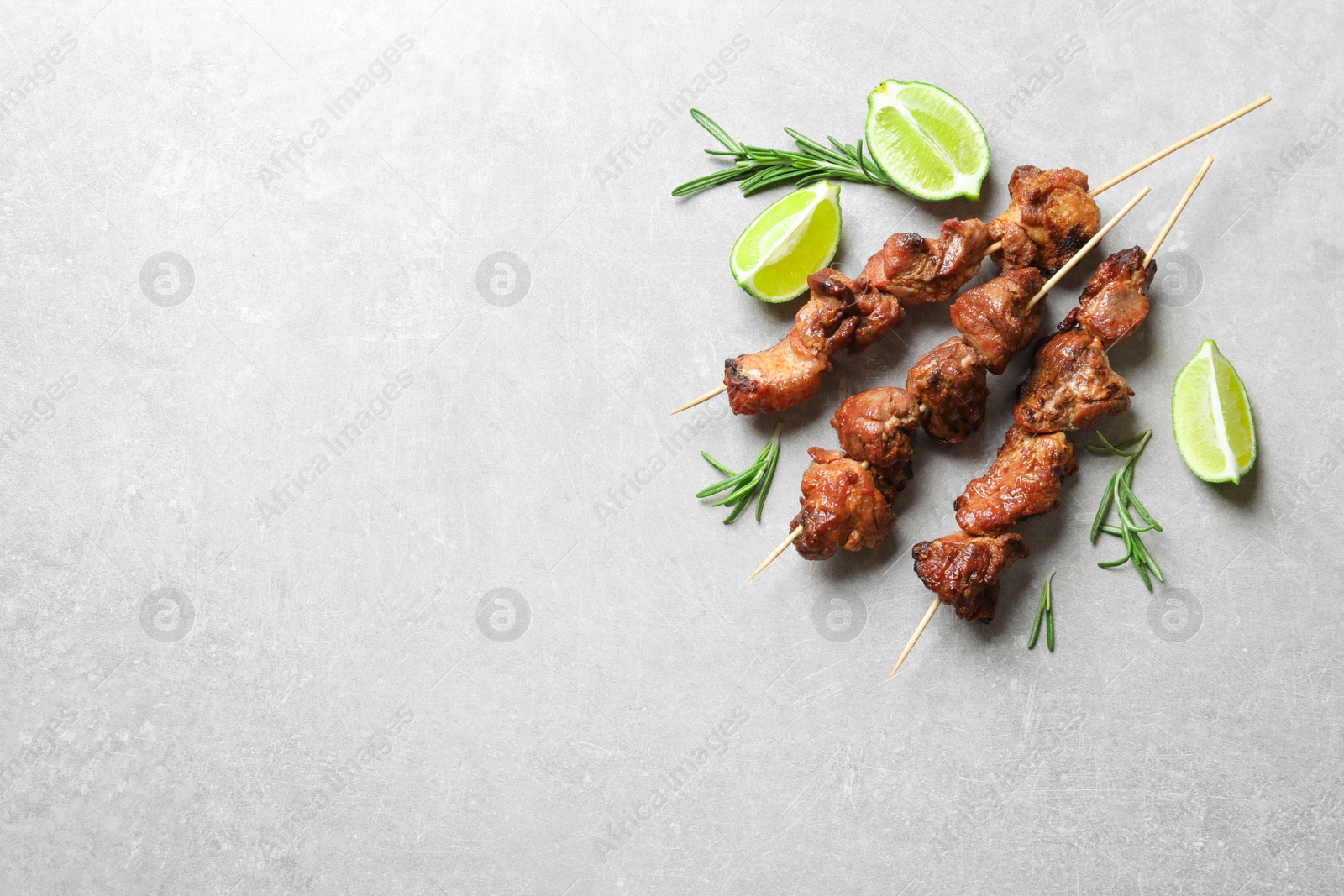 Photo of Delicious barbecued meat with rosemary and lime on grey background, top view. Space for text