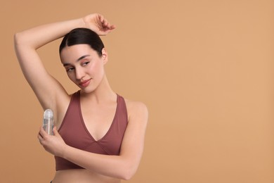 Beautiful woman applying deodorant on beige background, space for text