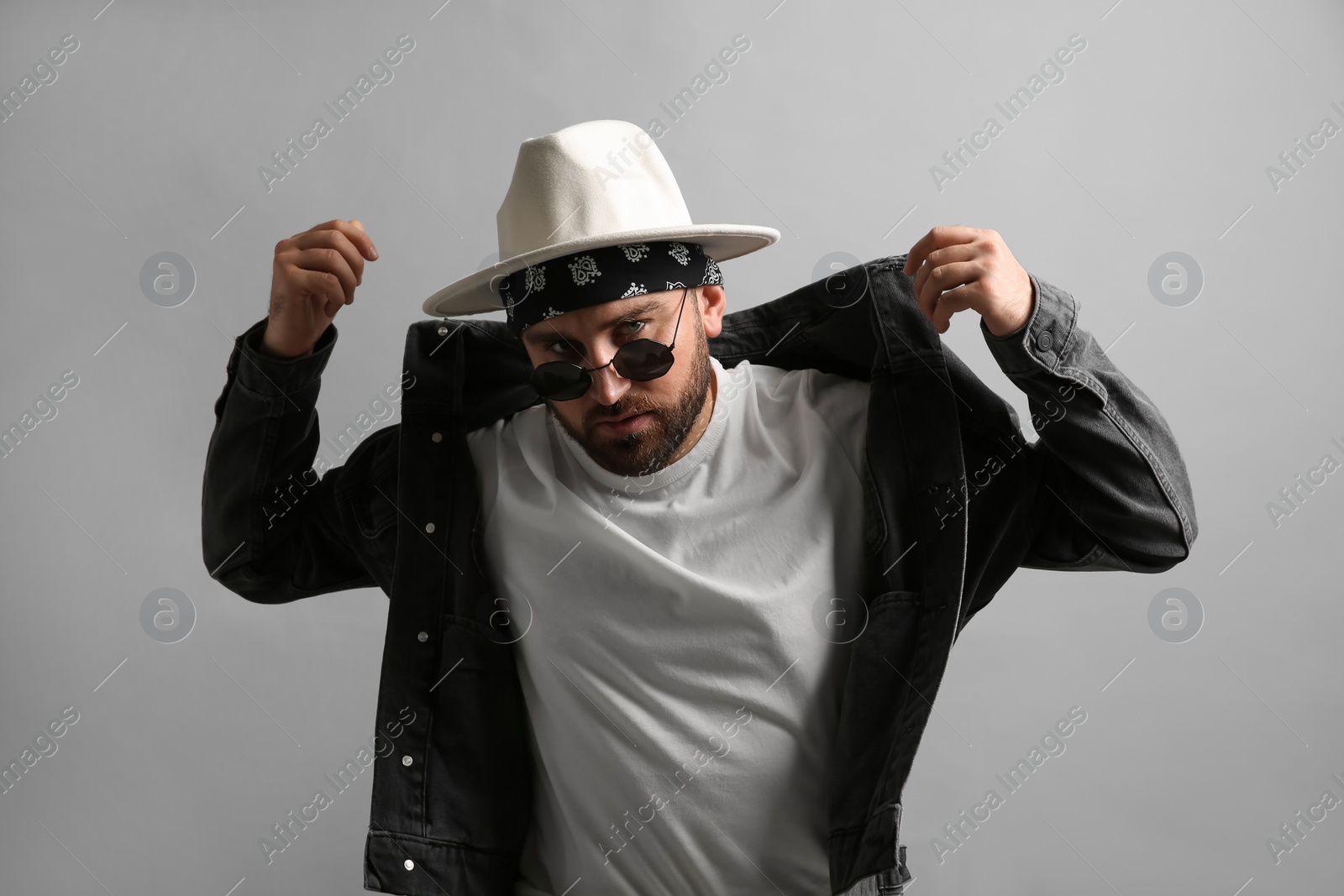 Photo of Fashionable young man in stylish outfit with bandana on grey background