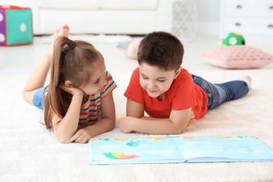 Photo of Cute little children reading book on floor in playing room