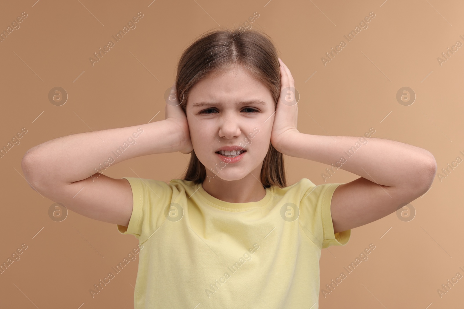 Photo of Hearing problem. Little girl suffering from ear pain on pale brown background
