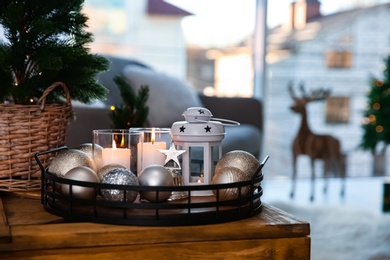 Photo of Burning candles, lantern and Christmas balls on wooden table indoors