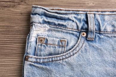 Photo of Stylish light blue jeans on wooden background, closeup of inset pocket