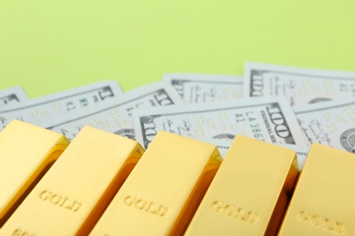 Photo of Gold bars and dollar bills on color background, closeup