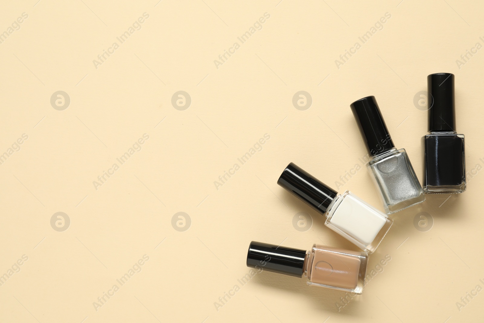 Photo of Bright nail polishes in bottles on beige background, flat lay. Space for text