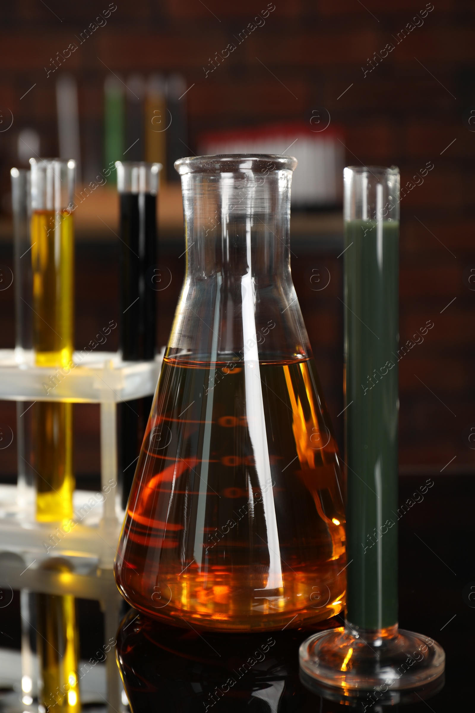 Photo of Laboratory glassware with different types of oil on black mirror table, closeup