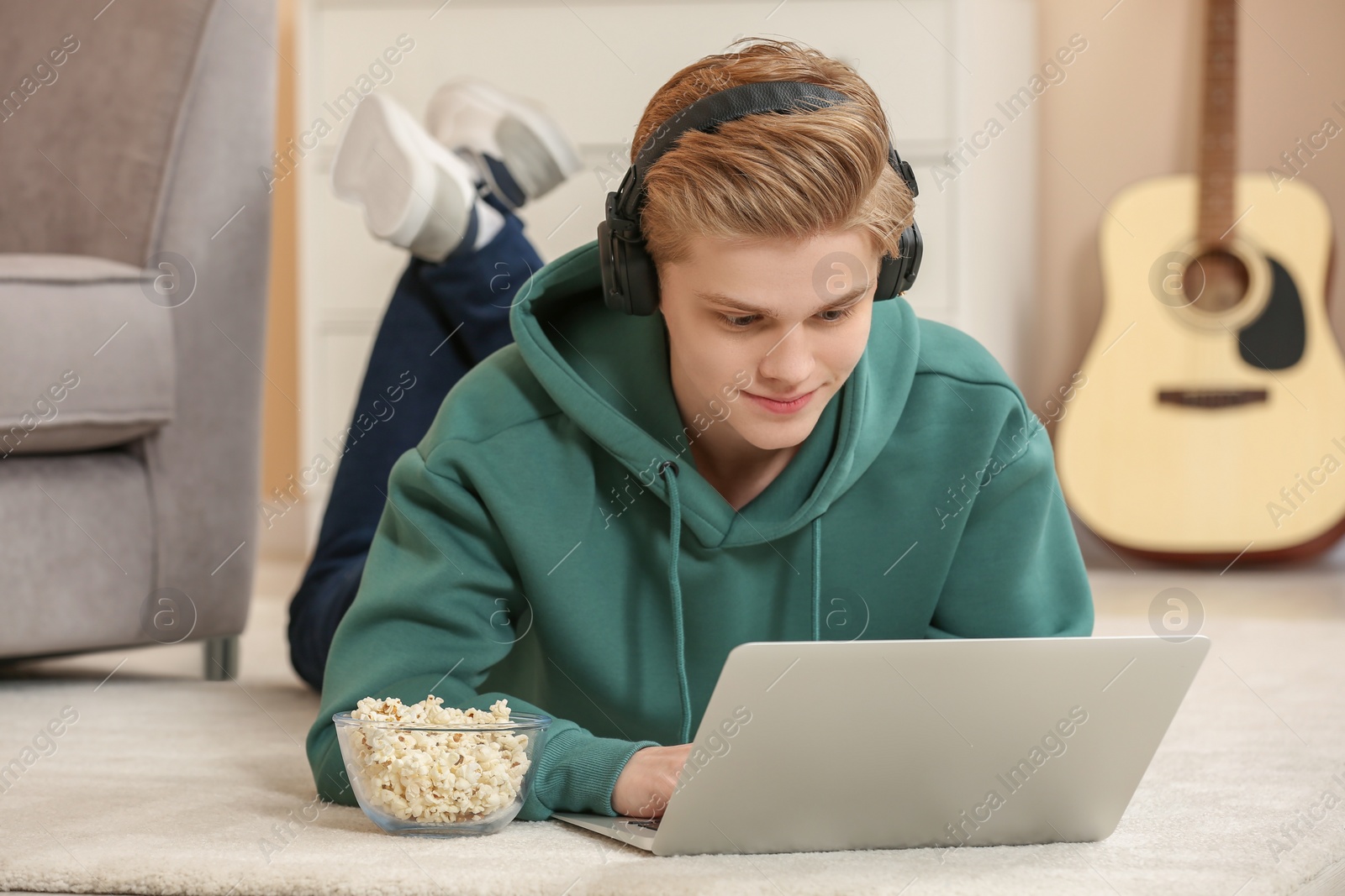 Photo of Teenage boy with headphones and popcorn using laptop at home