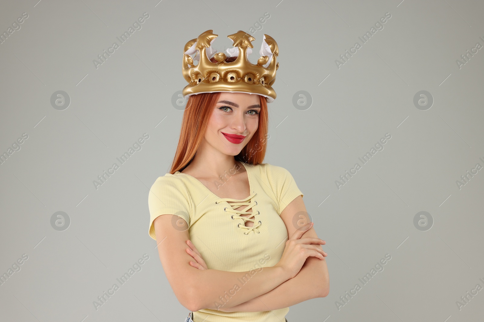 Photo of Beautiful young woman with inflatable crown on light grey background, space for text