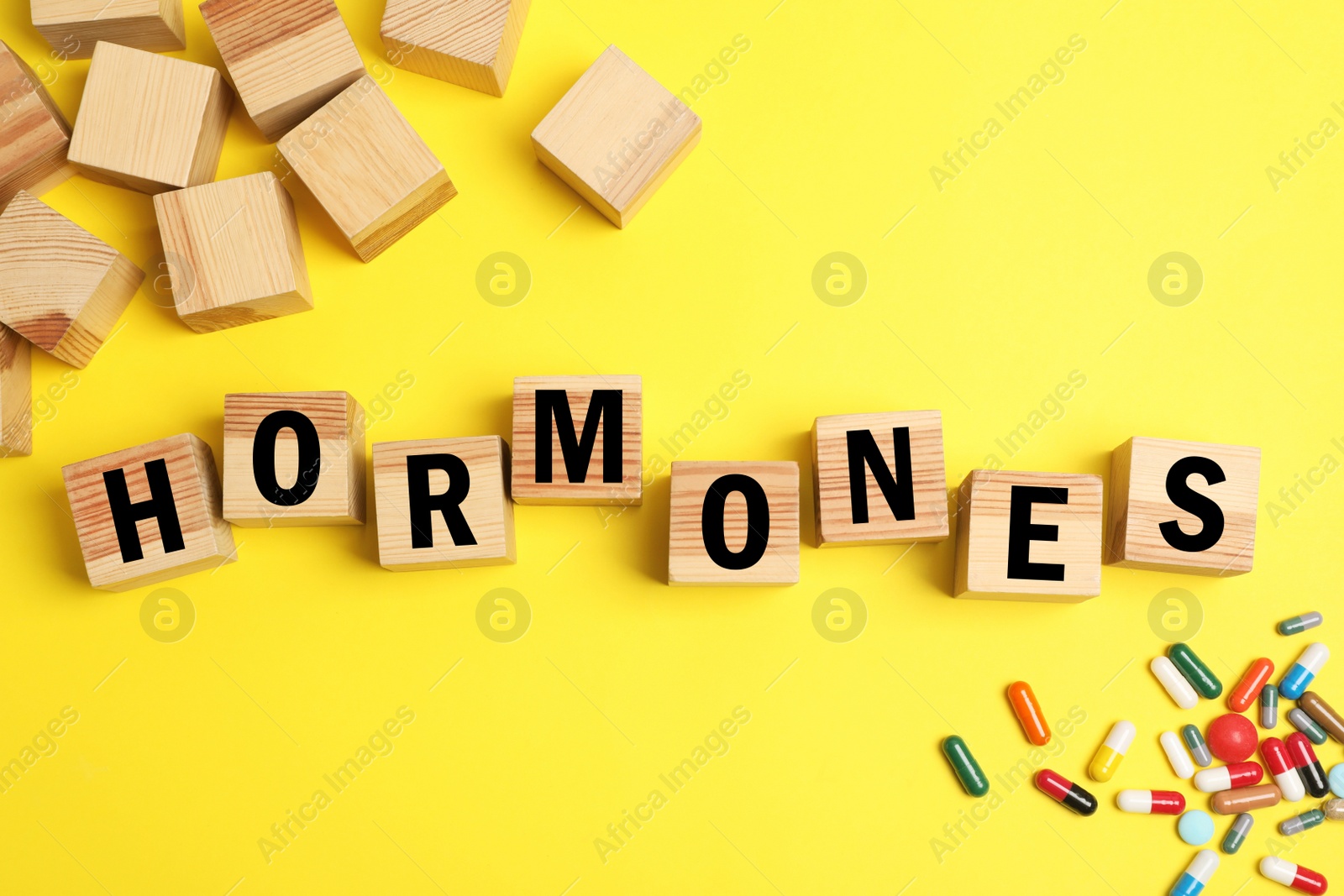 Photo of Word Hormones made of wooden cubes with letters and pills on yellow background, flat lay