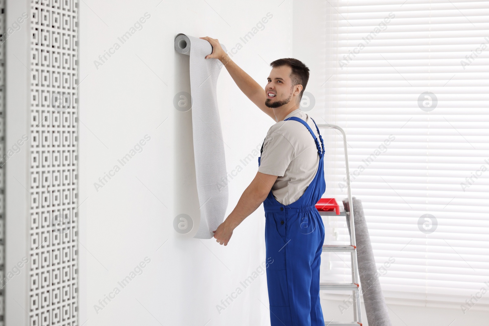 Photo of Man hanging stylish gray wallpaper in room