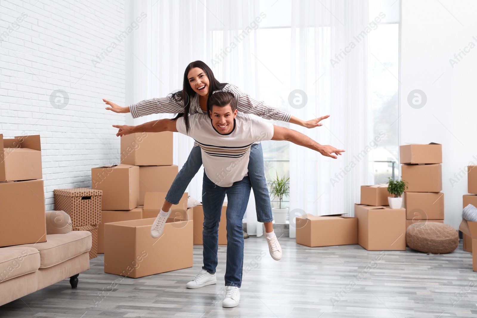 Photo of Happy couple having fun in room with cardboard boxes on moving day