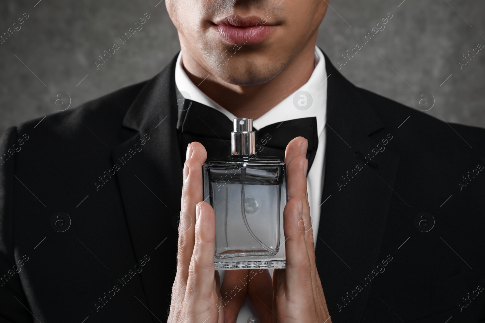 Photo of Handsome young man with bottle of perfume on grey stone background, closeup