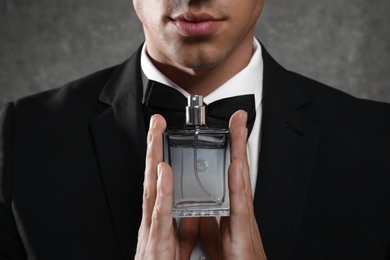 Handsome young man with bottle of perfume on grey stone background, closeup