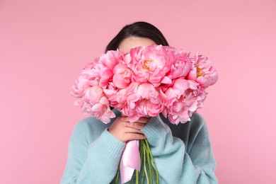 Photo of Young woman covering her face with bouquet of peonies on pink background