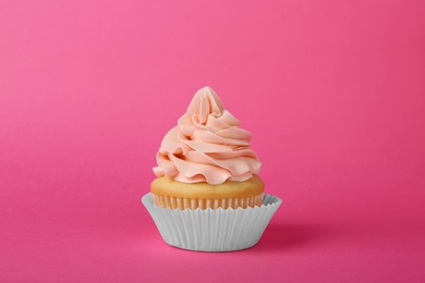 Tasty cupcake decorated with cream on pink background