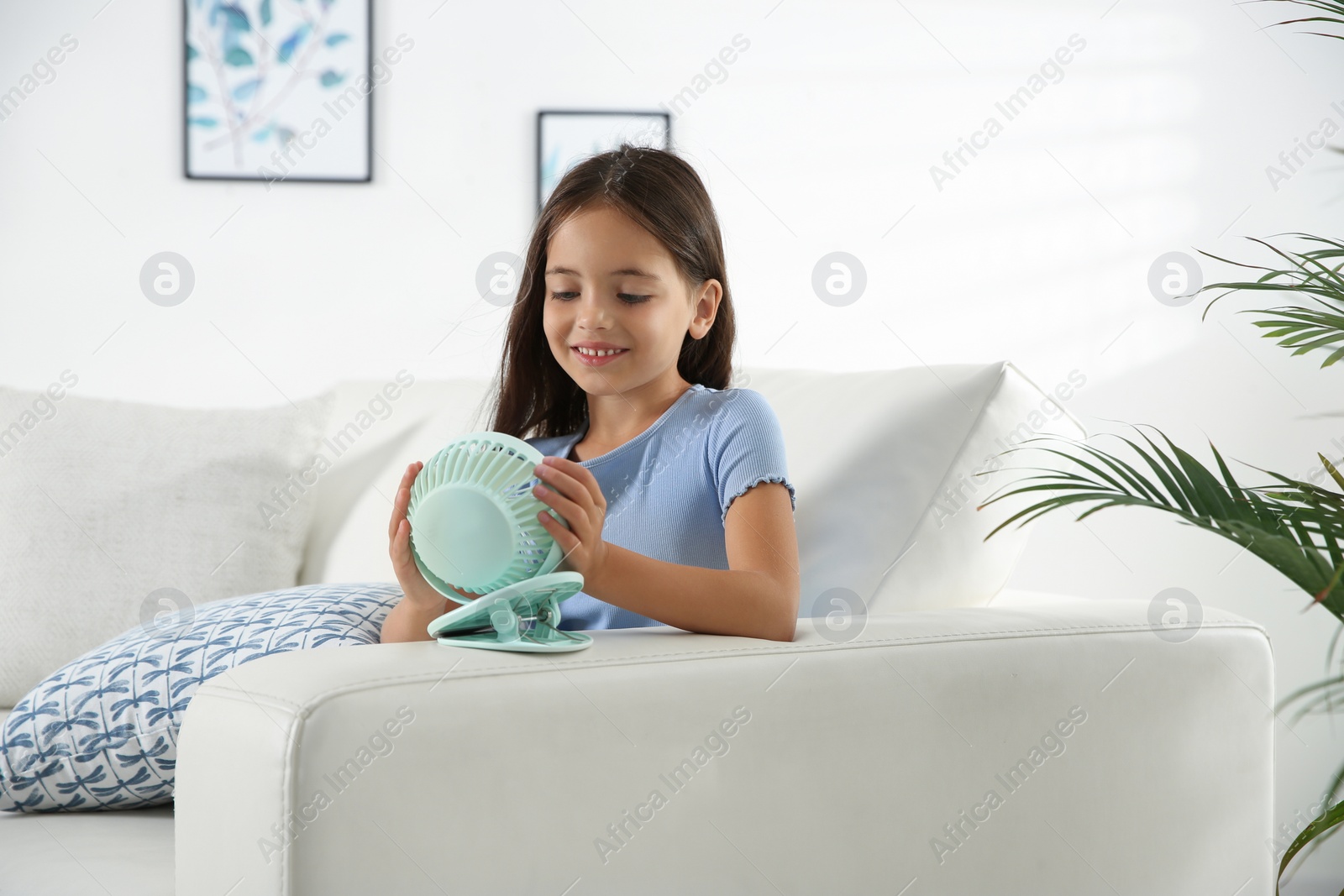 Photo of Little girl enjoying air flow from portable fan at home. Summer heat