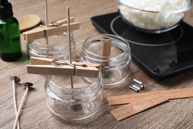 Photo of Glass jars with wicks and clothespins as stabilizers on wooden table. Making homemade candles