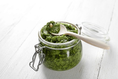 Jar of pesto sauce with spoon on wooden table