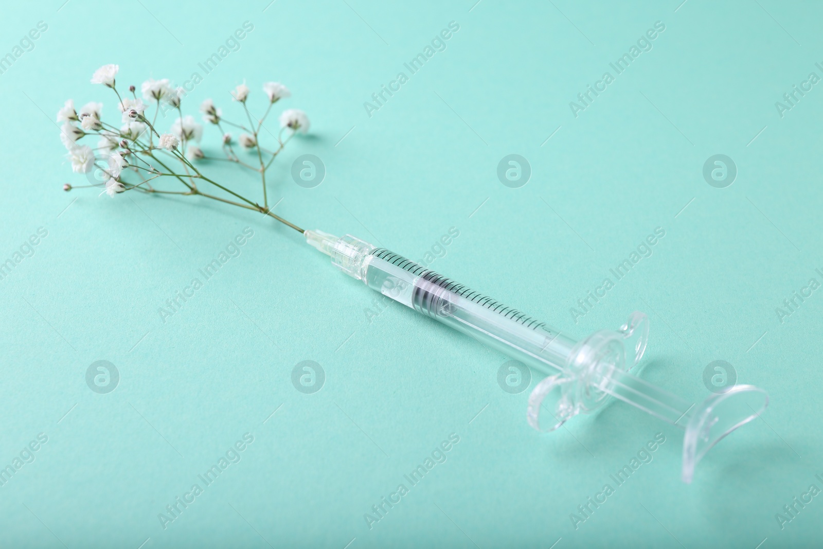 Photo of Cosmetology. Medical syringe and gypsophila on turquoise background