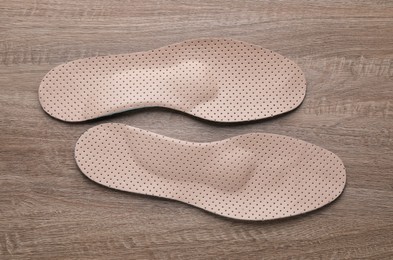 Photo of Beige orthopedic insoles on wooden background, flat lay