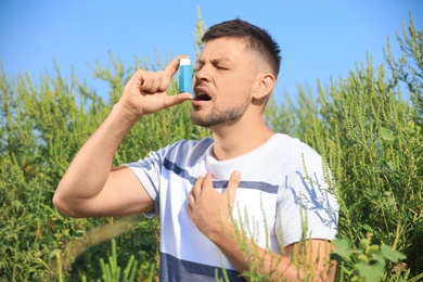 Photo of Man with inhaler suffering from ragweed allergy outdoors on sunny day