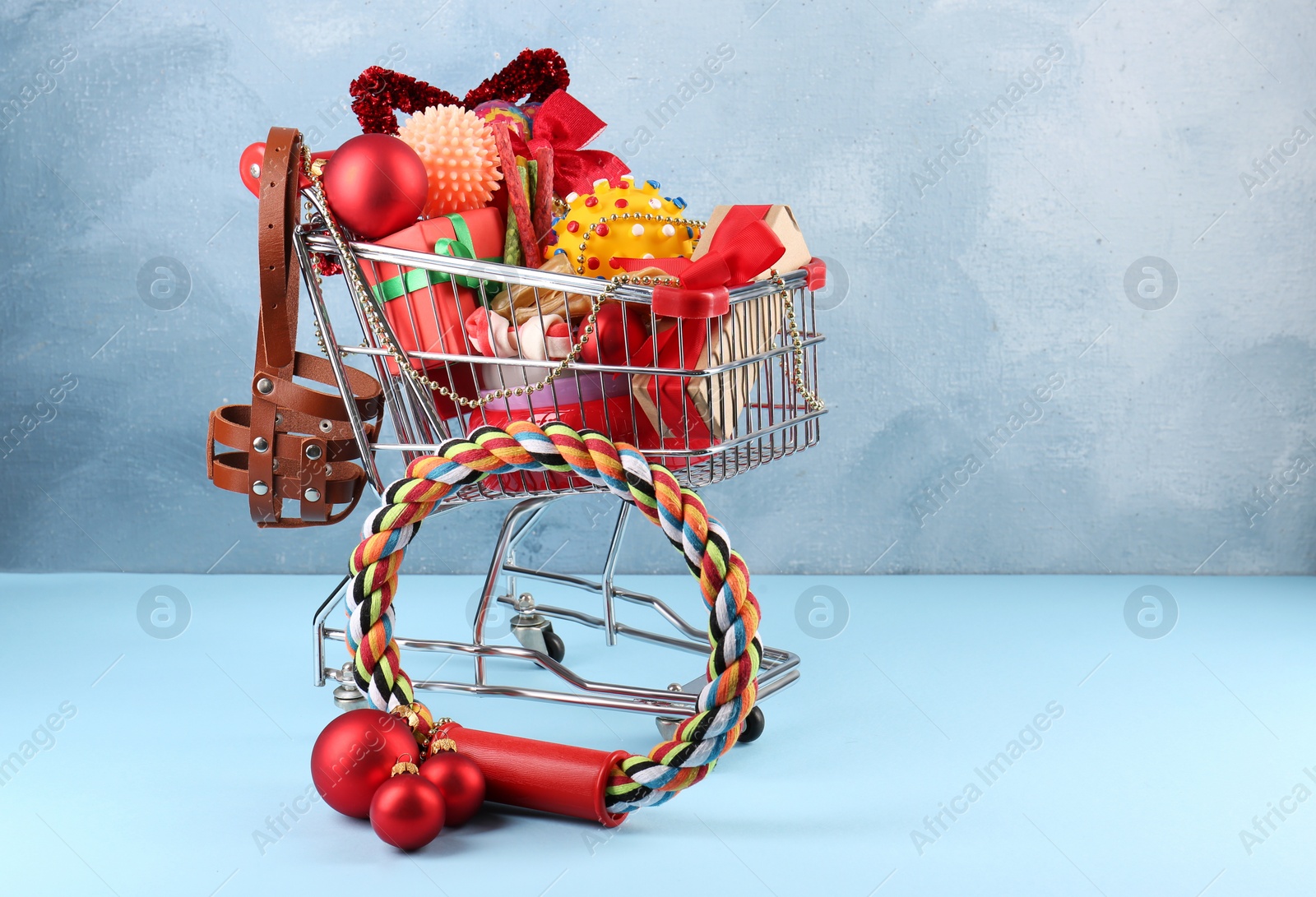 Photo of Small shopping cart with different pet goods and Christmas gifts on light blue background, space for text. Shop assortment