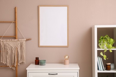 Photo of Empty frame hanging on pale rose wall over chest of drawers in room. Mockup for design