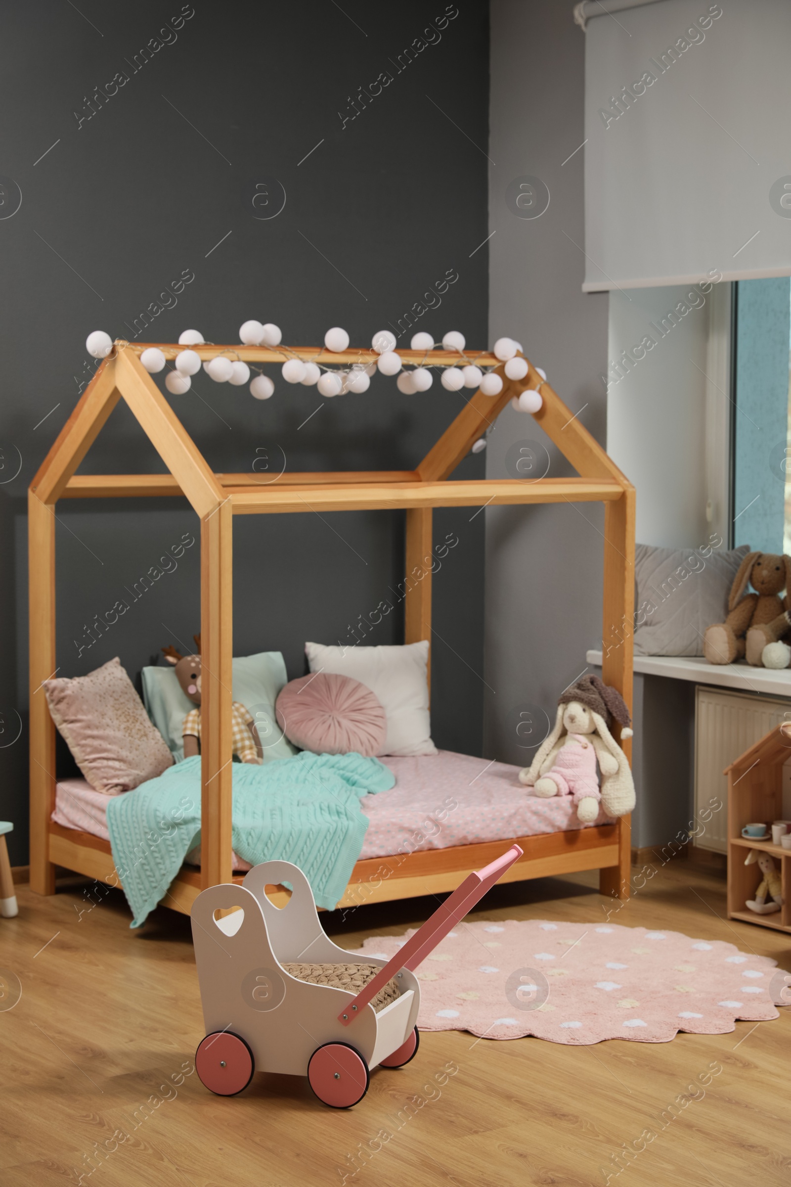 Photo of Stylish child room interior with wooden bed in shape of house and toys