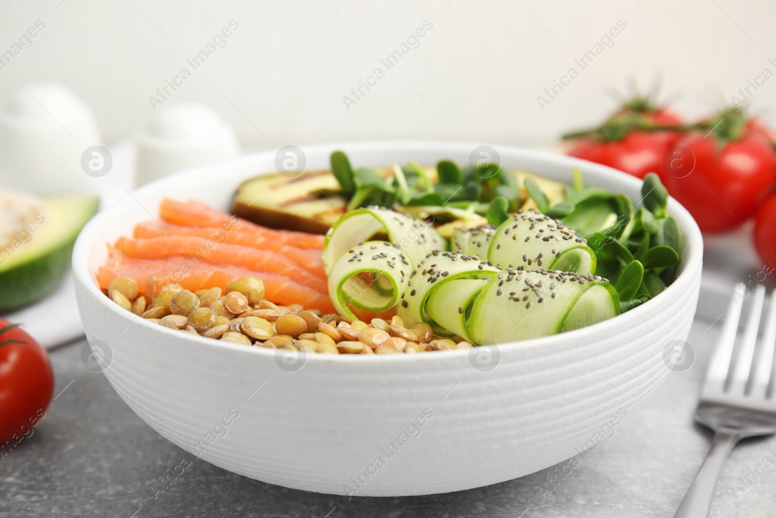 Photo of Delicious lentil bowl with salmon, avocado and cucumber on grey table